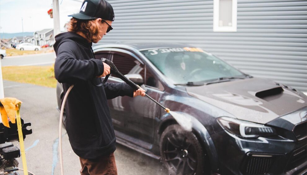 An image depicting a man washing a car as the American car wash industry blooms using water-efficient technology and eco-friendly cleaning products