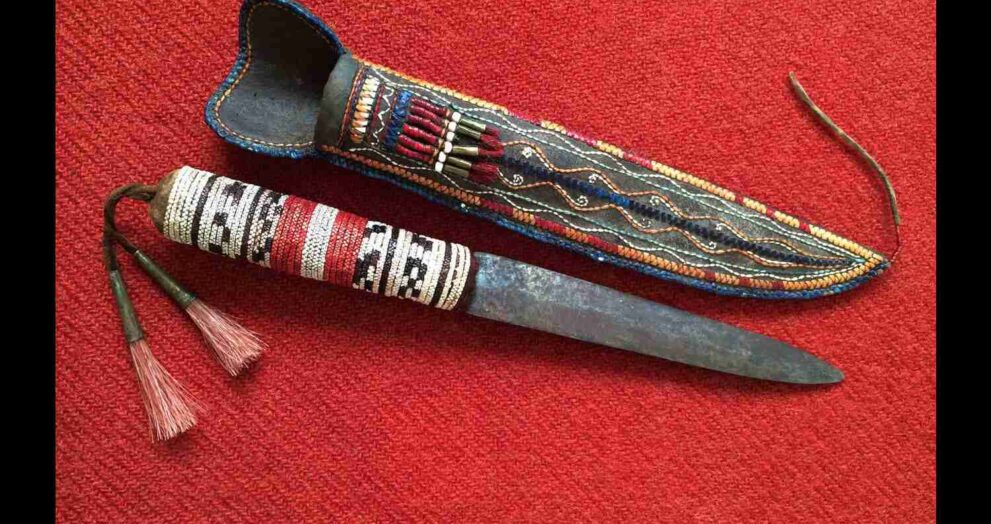A Native American knife with a decorative handle, displayed on a traditional woven mat.