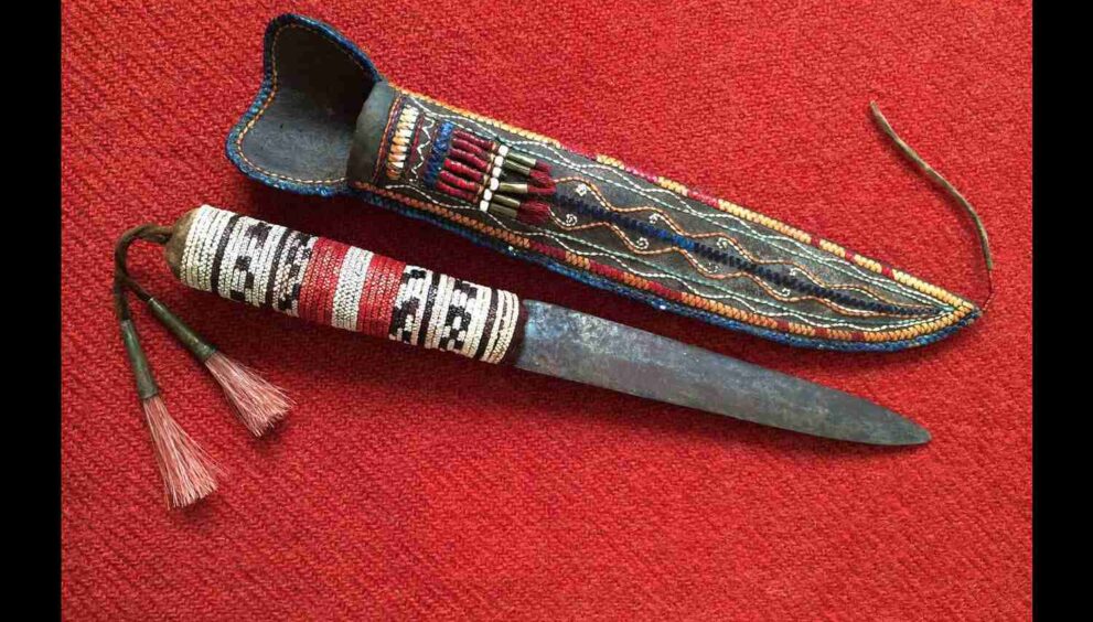 A Native American knife with a decorative handle, displayed on a traditional woven mat.