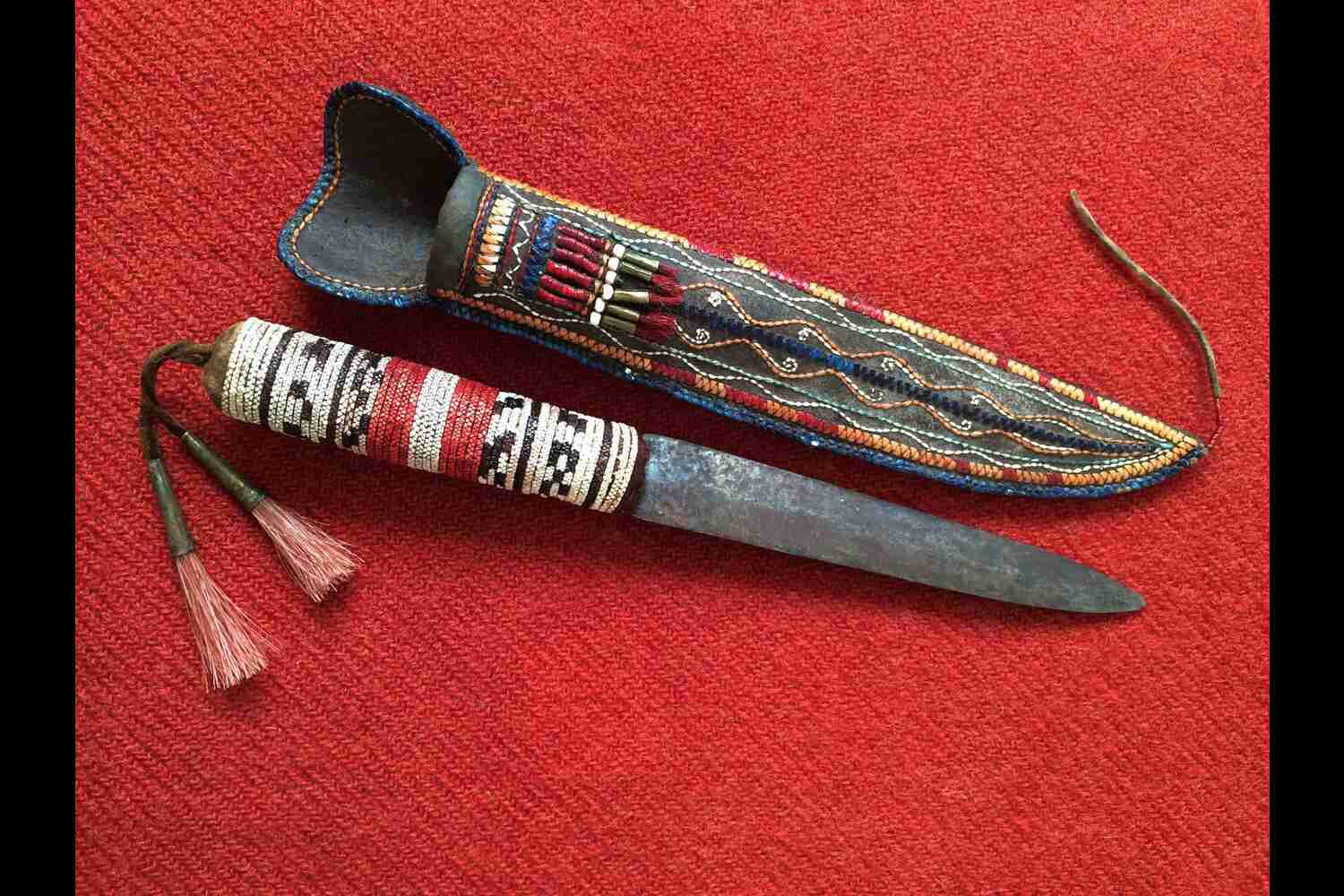 A Native American knife with a decorative handle, displayed on a traditional woven mat.