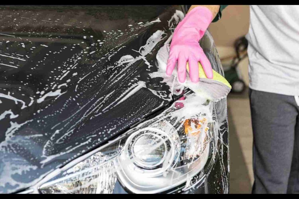 Image of a person hand-washing a car with soapy water and a sponge.
