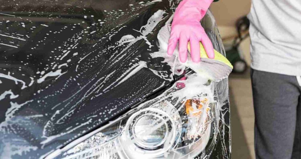 Image of a person hand-washing a car with soapy water and a sponge.