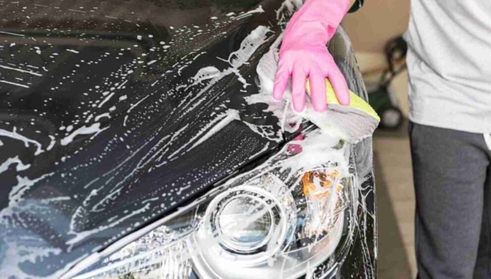 Image of a person hand-washing a car with soapy water and a sponge.