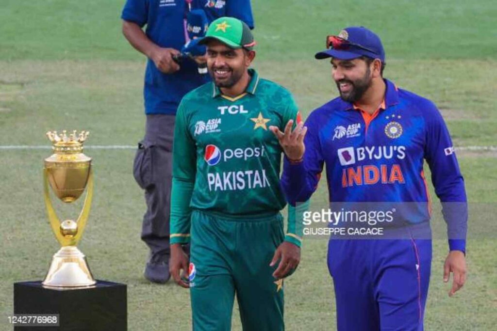 Two cricket players from Pakistan and India standing on a field with a trophy behind them.