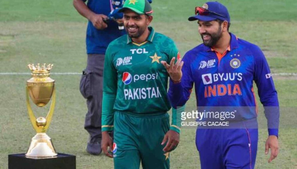 Two cricket players from Pakistan and India standing on a field with a trophy behind them.